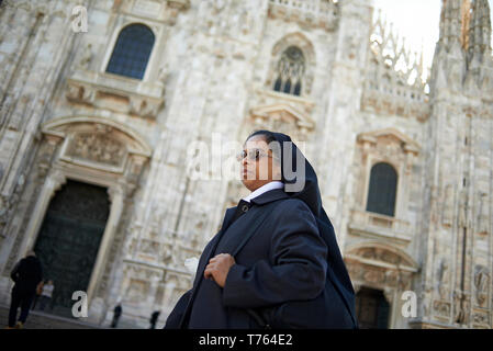 Elderly catholic nun walking down the street in the city centre of Milan in front of Duomo cathedral in summer sunshine Stock Photo