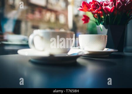 Two cups of coffee on table in cafe by window near vase with bouquet of pink tulips on sunny morning. Stock Photo