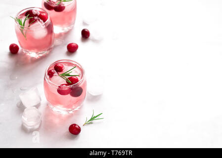 Cranberry Vodka Cocktail with ice cubes and rosemary on white marble background, copy space. Homemade alcohol cocktail with cranberries. Stock Photo
