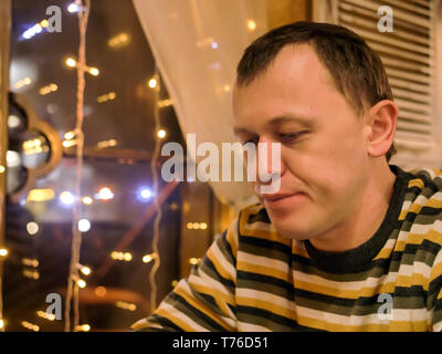 A young man in a striped sweater sits in the evening in a cafe near the window Stock Photo