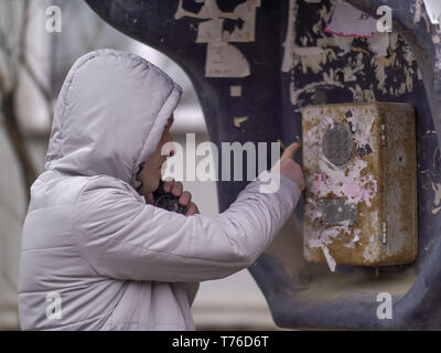 A man in a light jacket in a hood is calling an old street payphone Stock Photo