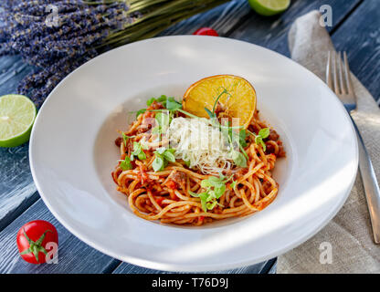 Classical Italian pasta bolognese, decorated with microgreen, grated parmesan and a slice of dry orange on a table on a sunny day, on a table with tom Stock Photo