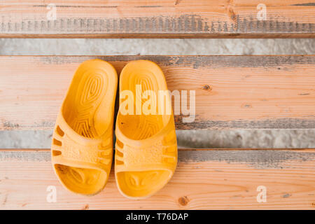 Yellow children's street Slippers on wooden bench top view. Stock Photo