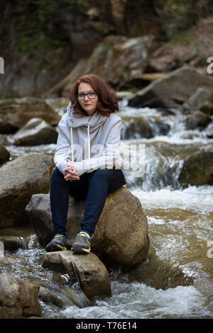 Young woman sitting on a rock in the middle of the river Stock Photo