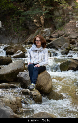 Young woman sitting on a rock in the middle of the river Stock Photo