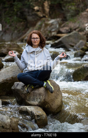 Young woman doing yoga zen on a rock in the middle of the river in a forest Stock Photo