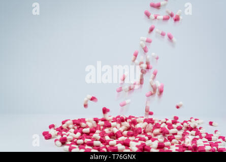 Selective focus on pink-white capsule pill fall down to white table. Antibiotic drug use with reasonable. Antibiotic drug resistance. Pharmaceutical Stock Photo