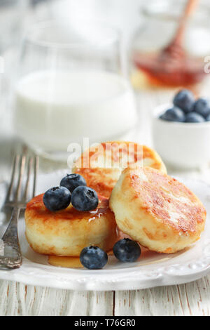 Cottage cheese pancakes, syrniki, curd fritters with fresh berries blueberry and honey in a white plate. Gourmet Breakfast. Selective focus Stock Photo