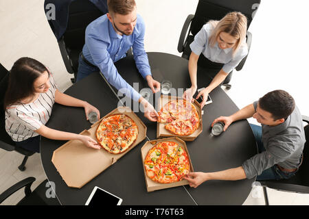 Young people eating pizza at table in office Stock Photo