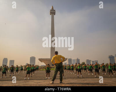 View of many men contestants  exercising at the National Monument  in Merdeka Square Jakarta, Indonesia before the annual run. The city skyline is beh Stock Photo