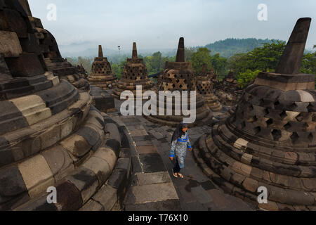 View looking down at woman walking on patio amidst short round columns at Borobudur Temple