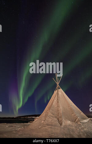 Drapery Aurora - curtain shaped northern lights dancing over a traditional sami tent partially covered in snow, Troms, Lyngen Alps, Northern Norway. Stock Photo