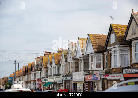 Southend-on-Sea, UK - March 2019: Row of traditional British houses in a slope street in the suburbs of Southend, with small shops and cars parked on  Stock Photo