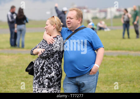 Pregnant woman standing on the lawn, at the city park, paunchy bodypositive man hugging her, people on a background. June 21,2018. Kyiv, Ukraine Stock Photo