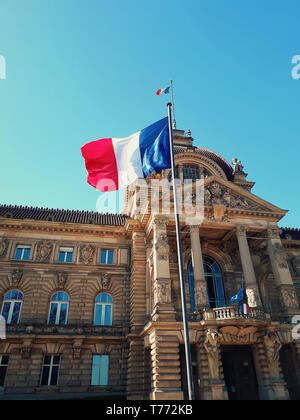 Wind blowing France flag on the mast against blue sky background in front of Palais du Rhin, Place de la Republique, Strasbourg, Alsace. Stock Photo