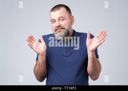 Bearded man in blue t-shirt shrugging shoulders Stock Photo