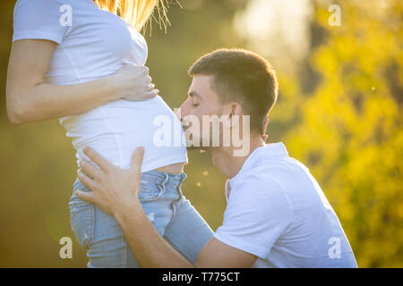 Happy couple expecting baby, happy man kissing belly of pregnant woman, young family and new life concept Stock Photo