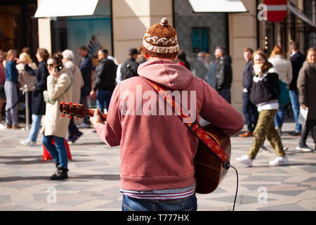 Street musician playing guitar in busy walking street with people walking by. Stock Photo