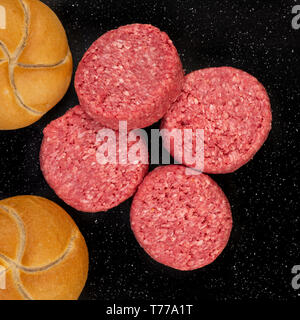 Fresh raw prime black Angus beef burger patties and bread buns on black stone background. Stock Photo