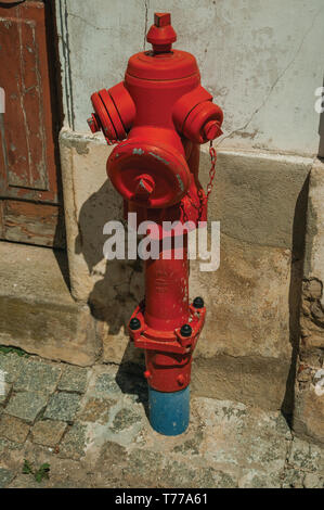 Red hydrant next to worn plaster wall on alley with deserted causeway at Portalegre. A little town near of Mamede Mountain Range in Portugal. Stock Photo