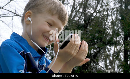 smiling teen boy with smart phone listening or talking in british park. teenager and social media concept. Stock Photo