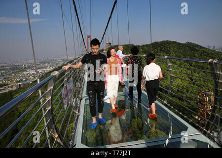 Wuxi, China's Jiangsu Province. 4th May, 2019. Tourists walk on a glass bridge at the Huaxi World Adventure Park in Huaxi Village of Jiangyin City, east China's Jiangsu Province, May 4, 2019. The 518-meter-long glass bridge hangs more than 100 meters above ground level at the park. It is made of panes of 35-mm-thick glass. Each glass can hold a maximum weight of 4.7 tonnes. Around 2,600 people can cross the bridge at a time. Credit: Xu Congjun/Xinhua/Alamy Live News Stock Photo