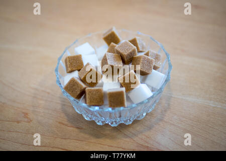 Brown sugar cubes and white sugar cubes in a glass bowl. Stock Photo