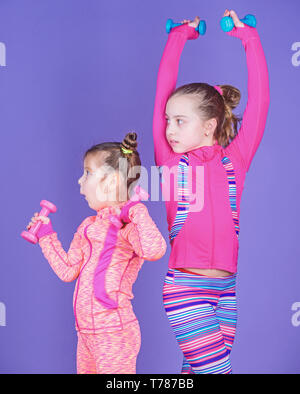 Healthy upbringing. Sporty babies. Following her sister. Girls cute kid exercising with dumbbells. Motivation and sport example concept. Toddler repeat exercise after sister. Sport exercises for kids. Stock Photo