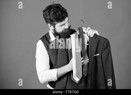 Shopping concept. Shop assistant or personal stylist service. Stylist advice. Matching necktie with outfit. Man bearded hipster hold neckties and formal suit. Guy choosing necktie. Perfect necktie. Stock Photo