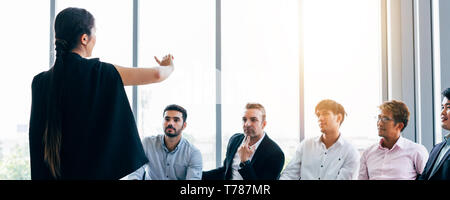 Elegant woman doing presentation for group of modern male coworkers having business meeting in light conference room Stock Photo