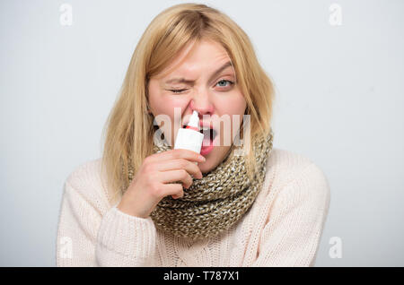 Clearing up. Sick woman spraying medication into nose. Unhealthy girl with runny nose using nasal spray. Cute woman nursing nasal cold or allergy. Treating common cold or allergic rhinitis. Stock Photo