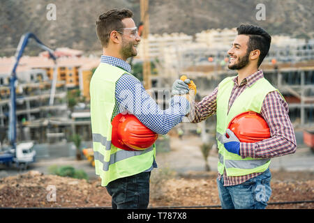 Young builders shaking hands making an agreement on costruction site - Workers reaching a deal and laughing Stock Photo