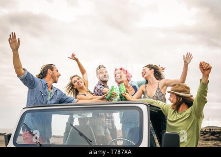 Group of happy friends cheering with beer in convertible car - Young people having fun drinking and making party during their road trip Stock Photo