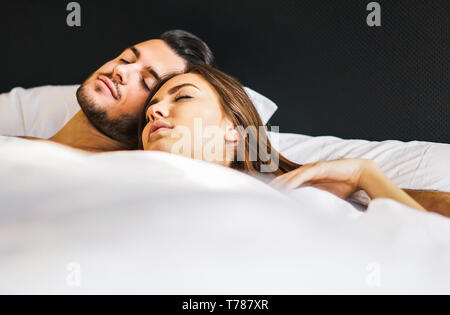 Loving young couple sleeping together in a bed with white sheets at home - Life's moments of people in love in the bedroom Stock Photo