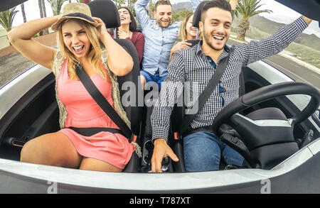 Happy friends having fun and dancing in convertible car in vacation - Young people making party in a cabrio auto during their road trip Stock Photo