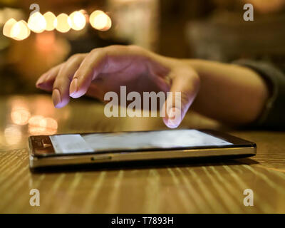 Woman uses a smartphone in the evening while sitting in a cafe Stock Photo