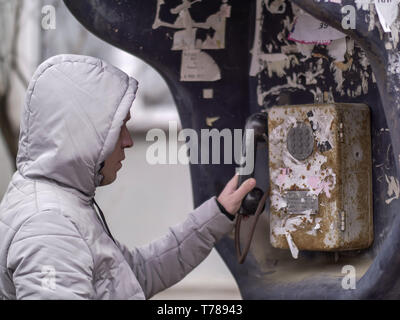 A man in a light jacket in the hood is calling an old payphone Stock Photo