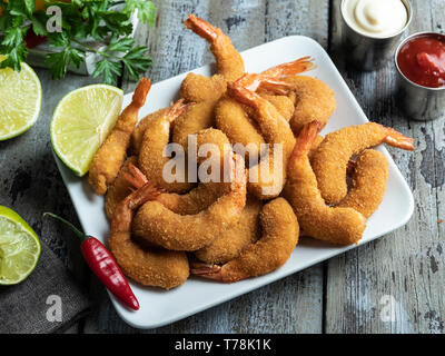 fried breaded shrimps served with lime on white plate on wooden table, delicious deep, red, white sauce Stock Photo