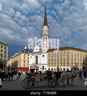 Horse and carriage in Michaelerplatz, with a sunlit St Michael's Church (Michaelerkirche) opposite in Vienna Old Town Stock Photo