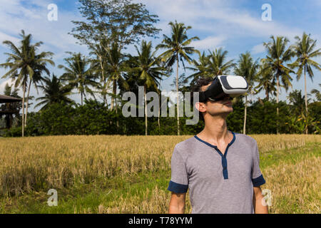 Young man wearing VR glasses in the tropical rice field Stock Photo