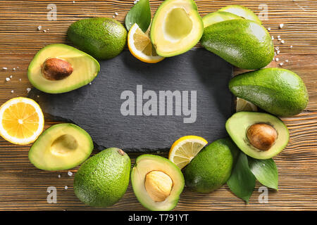 Frame made of ripe avocados and slate plate on wooden background Stock Photo