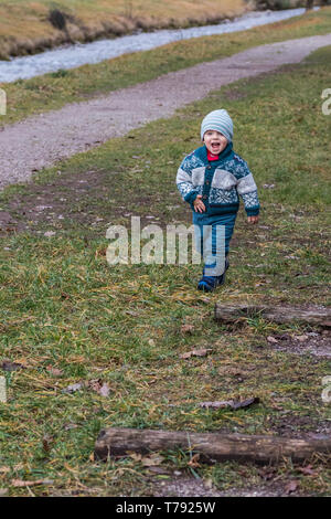 A toddler, dressed warm for the cooler weather, is seen joyfully smiling and walking. Stock Photo