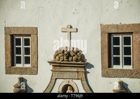 Skulls and cross carved in stone between windows embellishing the facade of church at Marvao. A medieval hamlet perched on a crag in Portugal. Stock Photo