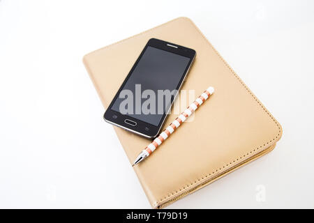 Black smart phone similar to leading brands sitting on top of gold compendium or diary with bronze and white striped pen. Useful for a contact me page Stock Photo