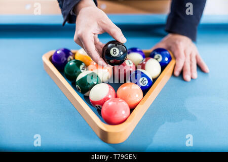 Close up of man hand holding eight billiard ball above pool balls in wooden triangle on snooker table. Stock Photo