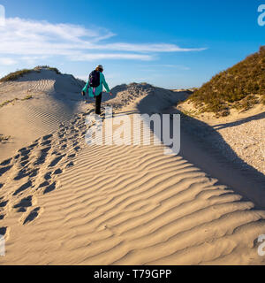 Woman with backpack hiking up sand dune on a sunny day on Isla Magdalena, Baja California Sur, Mexico. Stock Photo