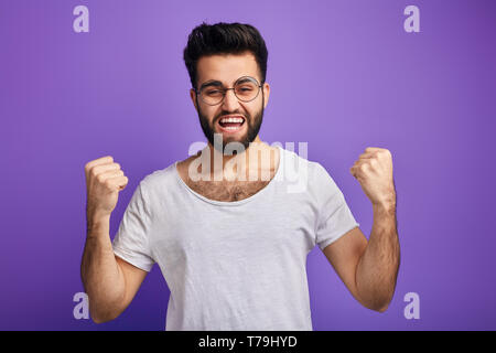 bearded man in glasses achieves hgoals won lottery, looks excited and amazed, celebrates victory of his team,clenches fists, feels triumph, screams wi Stock Photo