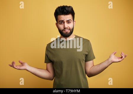 Unsure doubtful bearded man wearing green T-shirt shrugging his shoulders in questioning gesture of uncertainty. close up photo. issolated green backg Stock Photo