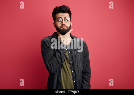 Serious attractive bearded scared stylish man touching chin and looking aside at camera. close up photo. isolated pink background. Stock Photo