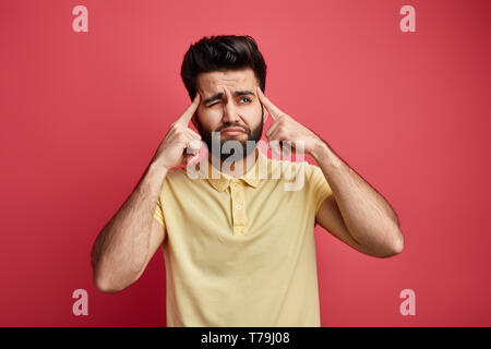 sad pensive thoughtfult young Indian man touching temples with fingers and looking up, asking to think before doing.let me think. Stock Photo